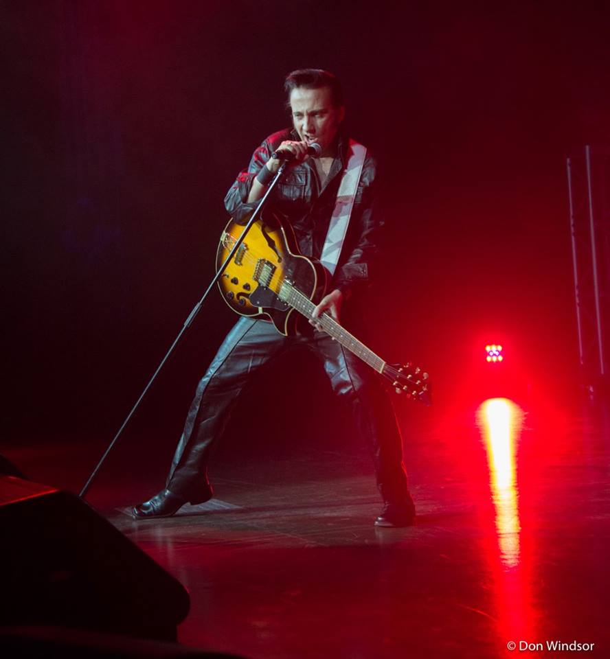 Adam T. Elvis performing on stage with a guitar